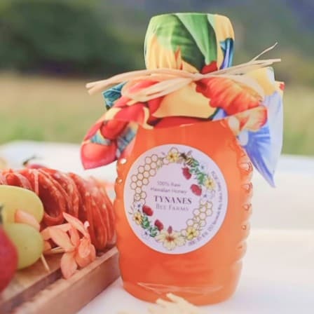 A bottle of Tynanes raw Hawaiian honey wrapped in tropical print fabric